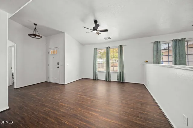 an empty room with wooden floor ceiling fan and windows