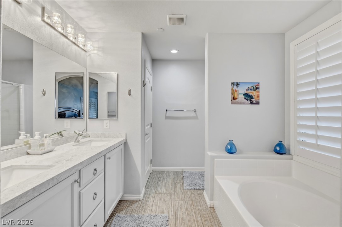 48 Jasmine Point Street Henderson, NV 89074 - Photo 40 of 62 A well-lit bathroom with a double vanity and soaking tub awaits, offering a tranquil retreat.