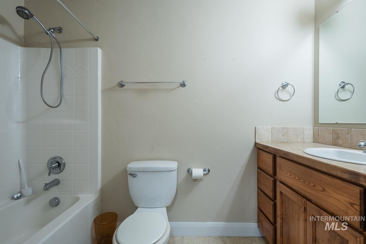 1186 East Observation Street Meridian, ID 83642 - Photo 28 of 33 Full bathroom featuring a white tub/shower combination with tiled surround, a white toilet, and a wood-finish vanity with a built-in sink and tiled countertop