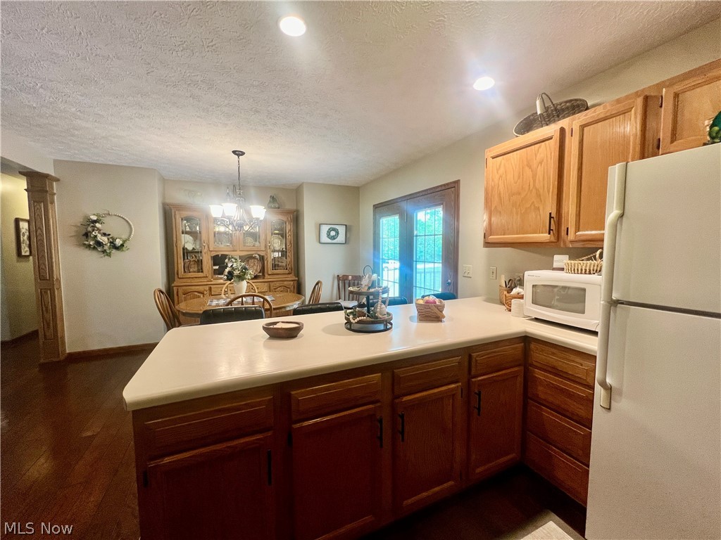 53360 High Ridge Road Bridgeport, OH 43912 - Photo 11 of 41 Kitchen with dark hardwood / wood-style flooring, a chandelier, kitchen peninsula, white appliances, and a textured ceiling