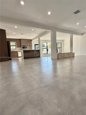 a view of an empty room with kitchen and window