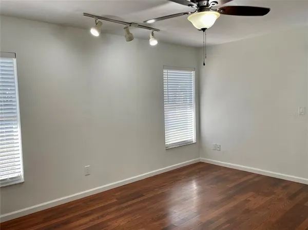 an empty room with wooden floor fan and windows