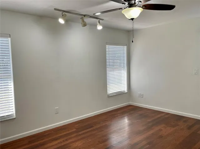an empty room with wooden floor fan and windows