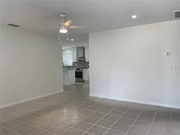an empty room with kitchen and chandelier fan