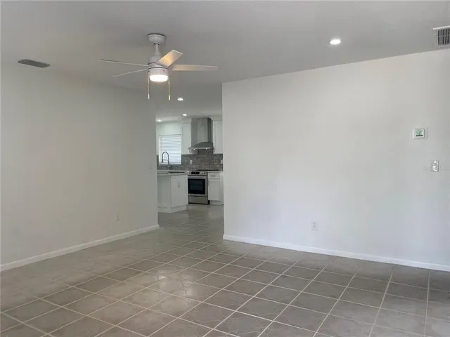 an empty room with kitchen and chandelier fan