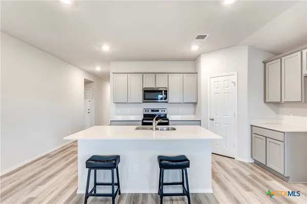 a kitchen with a sink a stove a refrigerator and white cabinets with wooden floor