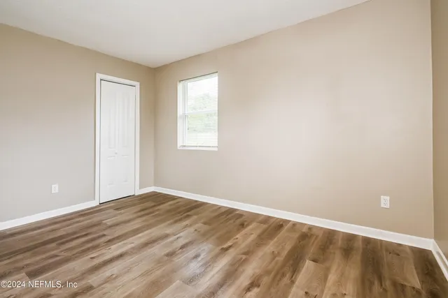 a view of an empty room with wooden floor and a window