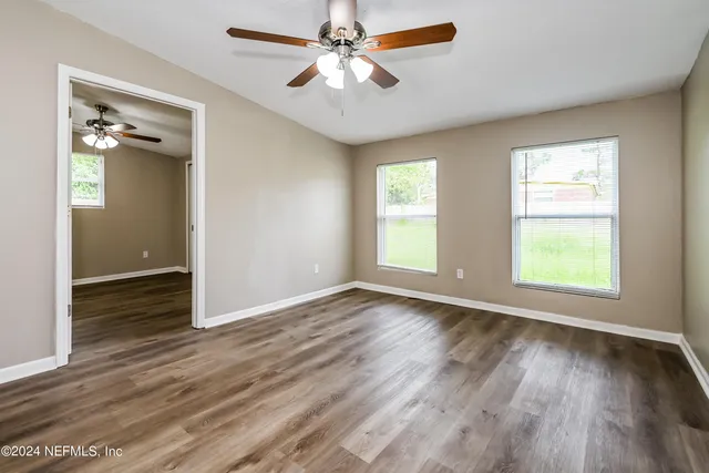 an empty room with wooden floor chandelier fan and windows