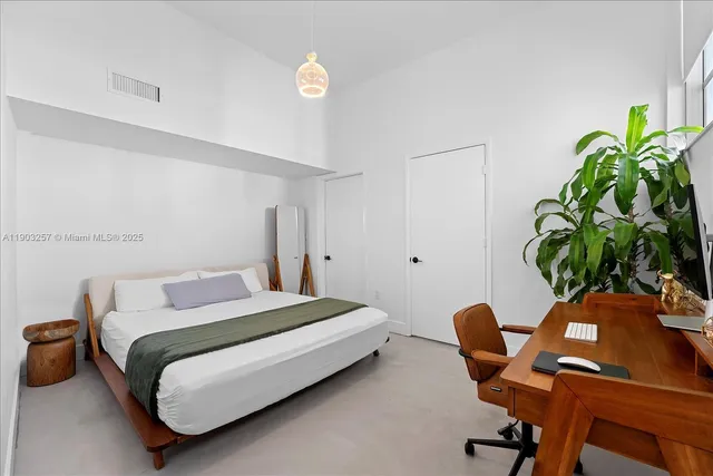 a bedroom with a bed table chair and a potted plant