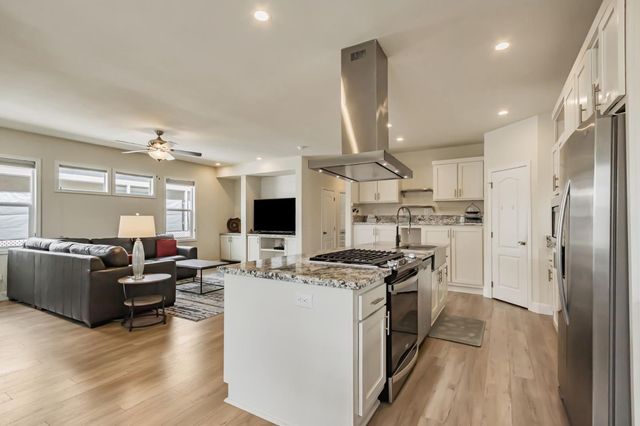 a kitchen with kitchen island stainless steel appliances a stove a refrigerator a sink dishwasher a oven with white cabinets and wooden floor