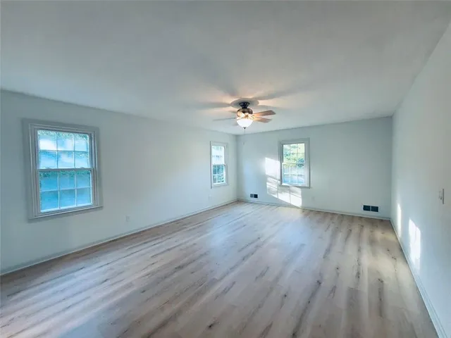 a view of an empty room with wooden floor and a ceiling fan