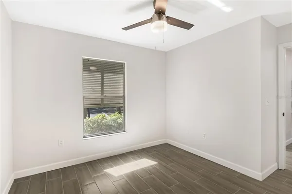 an empty room with wooden floor chandelier fan and windows