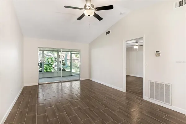 an empty room with wooden floor fan and windows