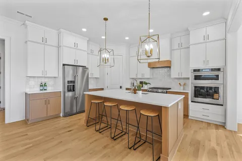 a kitchen with stainless steel appliances granite countertop a sink a stove a refrigerator and white cabinets with wooden floor