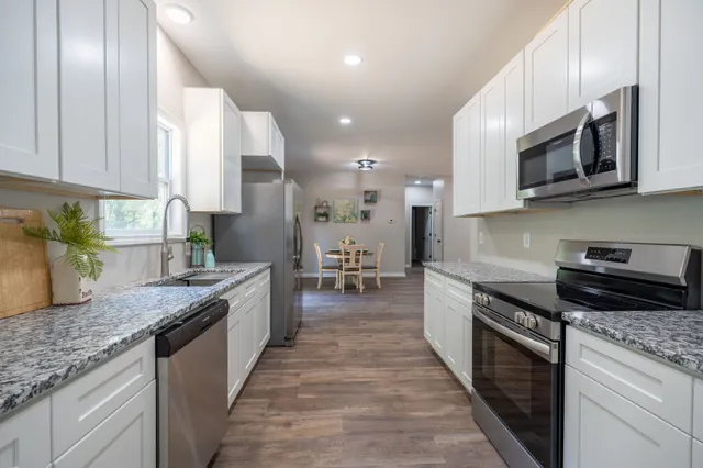 a large kitchen with stainless steel appliances granite countertop a stove top oven a sink dishwasher a microwave oven and a granite counter tops with wooden floors