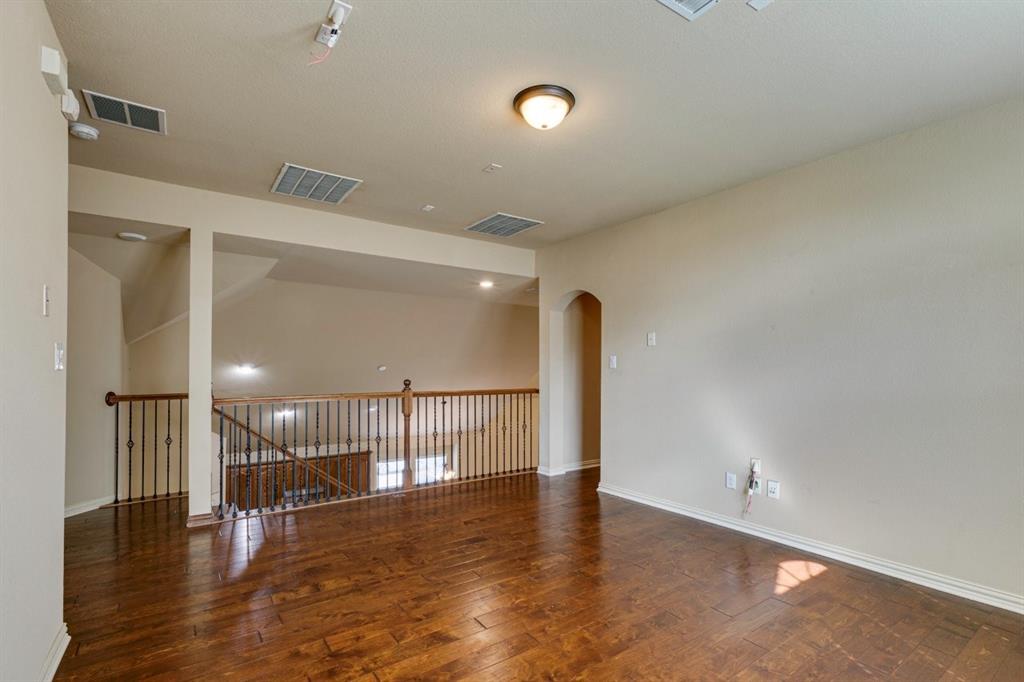 1522 Blue Jay Road Garland, TX 75043 - Photo 26 of 32 Spacious loft area featuring rich wood-finish flooring, a wrought iron and wood balustrade, an arched doorway, and recessed lighting