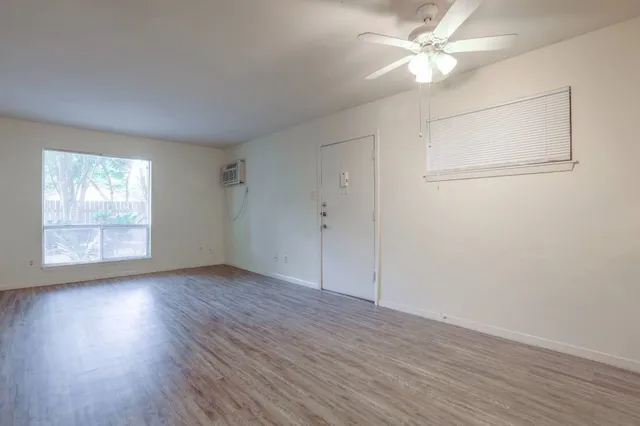 an empty room with wooden floor fan and windows