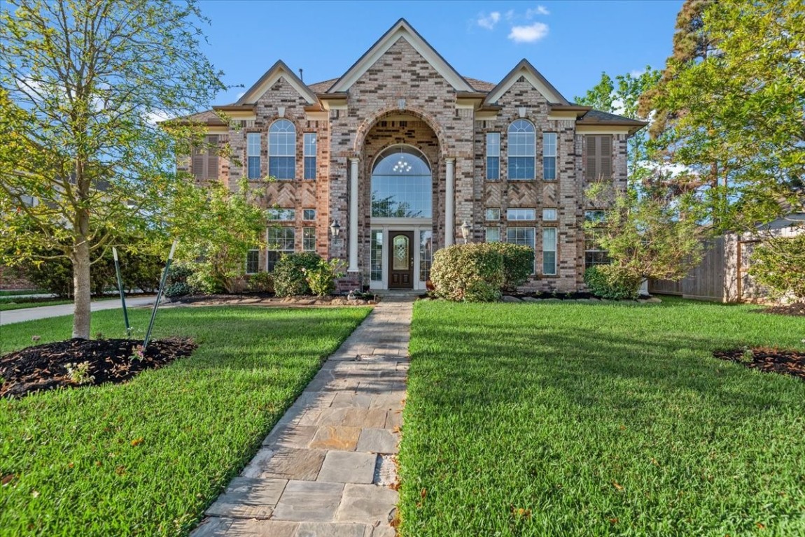Beautiful two-story brick home with large arched windows and a welcoming front entrance. It's surrounded by a well-maintained lawn and mature landscaping, offering great curb appeal.