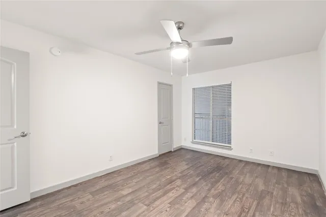 an empty room with wooden floor ceiling fan and windows