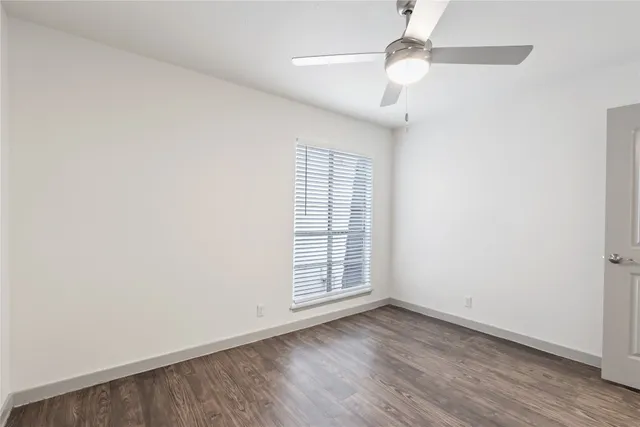 an empty room with wooden floor chandelier fan and windows