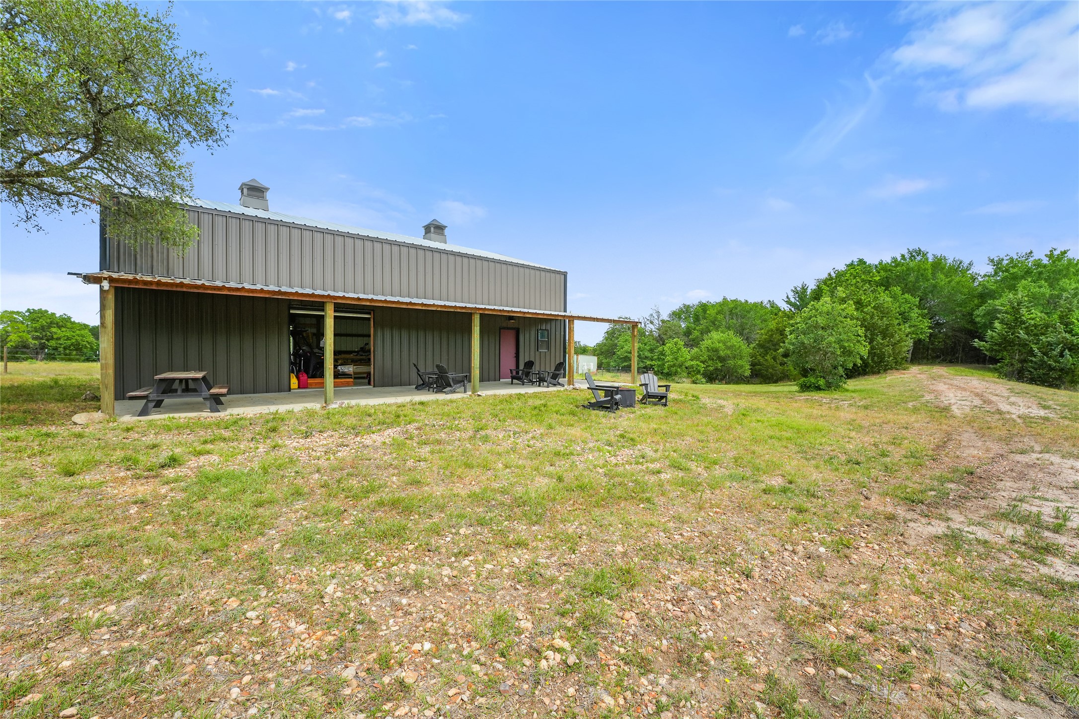 5837 FM 180 Road Ledbetter, TX 78946 - Photo 1 of 16 Timber frame metal barn with a covered patio set on 13+ Wildlife Exempt acres! Fire pit, bbq, picnic table and seating areas, surrounded by trees, offering a private and serene outdoor space.