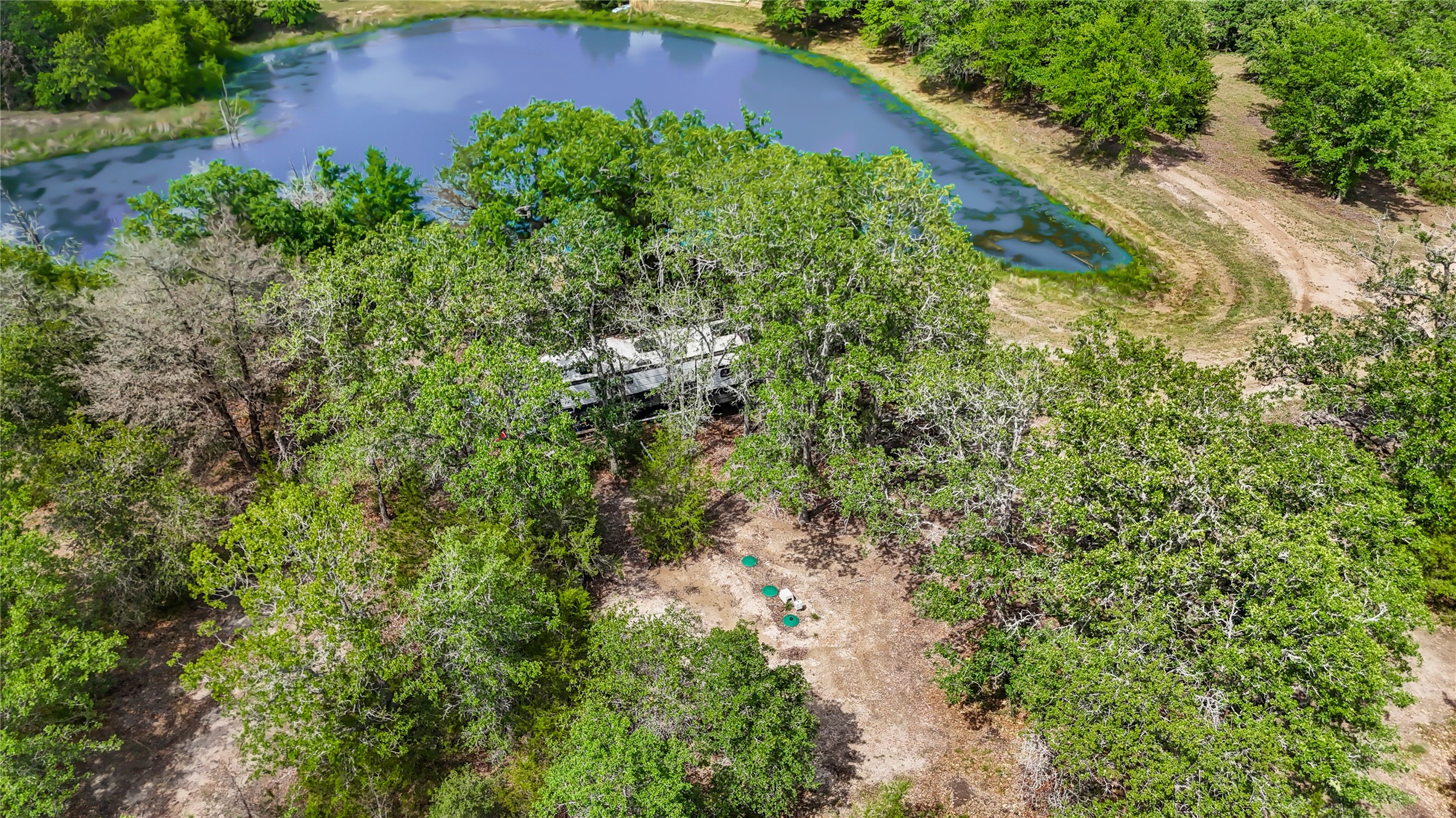 5837 FM 180 Road Ledbetter, TX 78946 - Photo 15 of 16 View of 2020 RV nestled in the trees by the pond. Currently serviced by the septic and well that have been put in place for the home site.