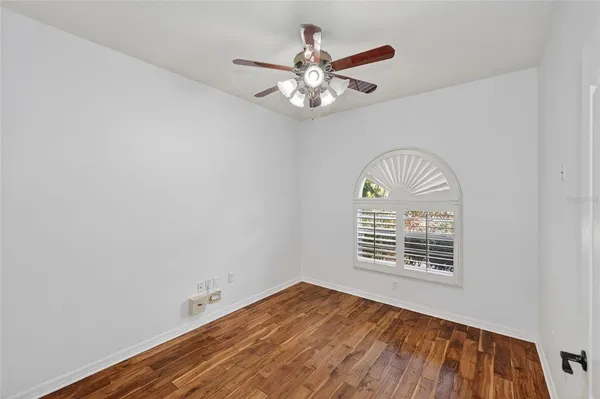 an empty room with wooden floor fan and windows