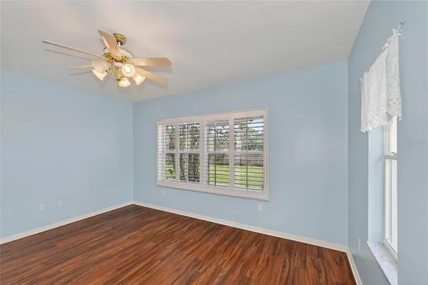 an empty room with wooden floor fan and windows