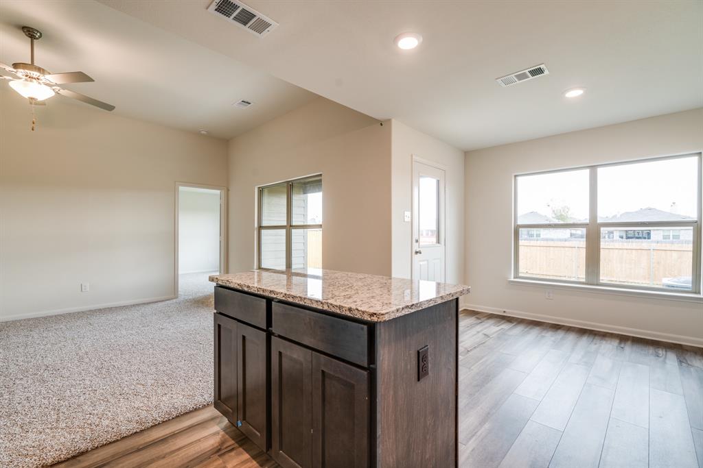 232 Micah Lane Ferris, TX 75125 - Photo 31 of 32 Kitchen with dark brown cabinetry, open floor plan, light stone countertops, a center island, and light wood finished floors