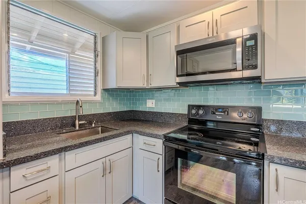 a kitchen with granite countertop a stove top oven cabinetry a sink and a window