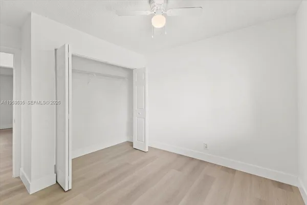 an empty room with a chandelier fan and wooden floor