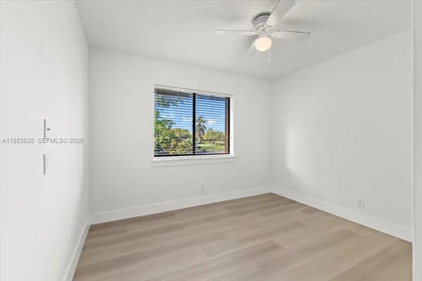 an empty room with wooden floor ceiling fan and window