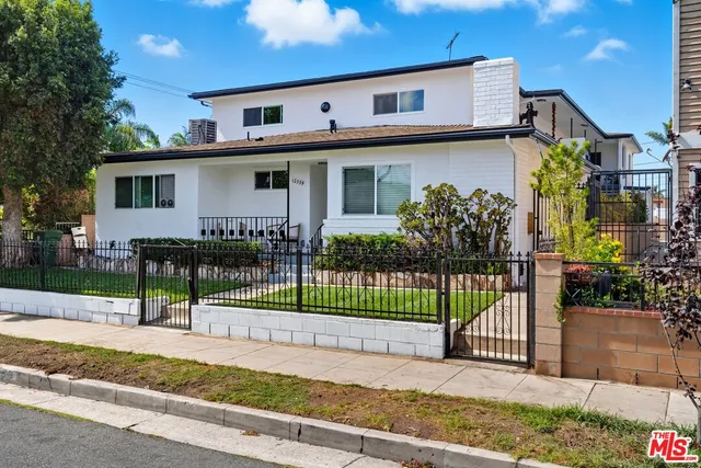 a view of a house in front of a yard with plants and a large tree