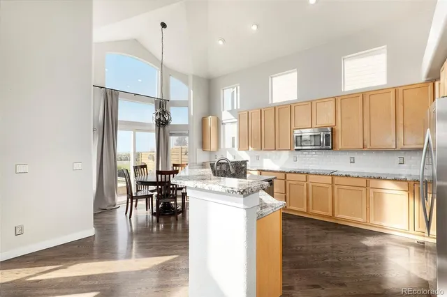 a kitchen with stainless steel appliances granite countertop a stove top oven a sink a dining table and chairs with wooden floor