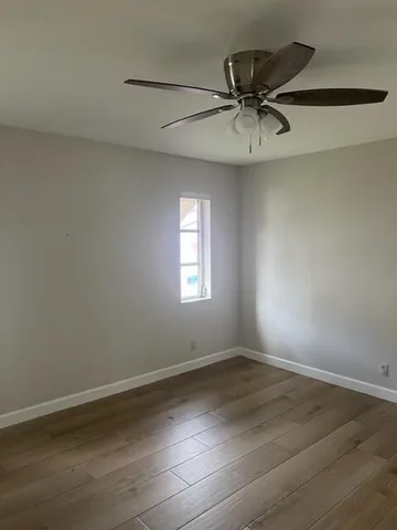 an empty room with wooden floor fan and windows