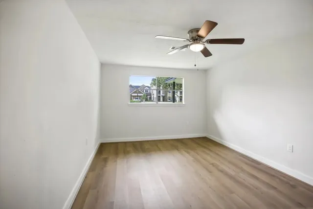an empty room with wooden floor ceiling fan and windows