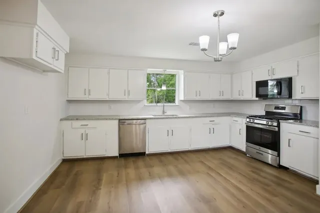 a kitchen with granite countertop white cabinets a stove a microwave oven a sink and dishwasher with wooden floor