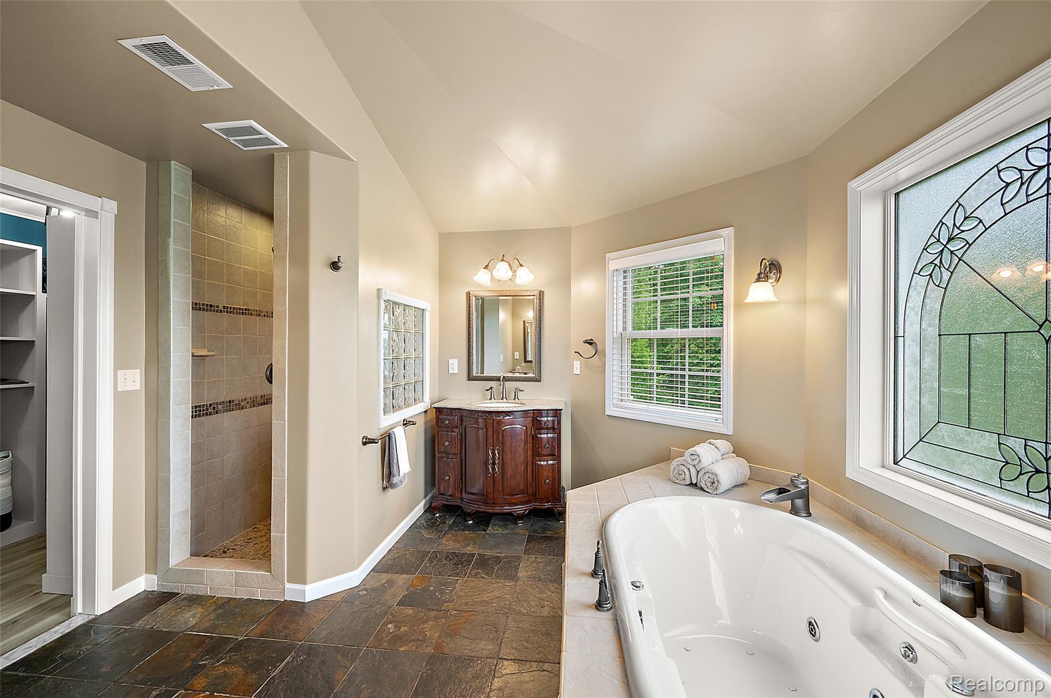 5035 Hidden Ridge Road Metamora, MI 48455 - Photo 32 of 65 Bathroom featuring a jetted soaking tub, walk-in shower with tile surround, and a vanity with a dark wood-finish cabinet and stone countertop