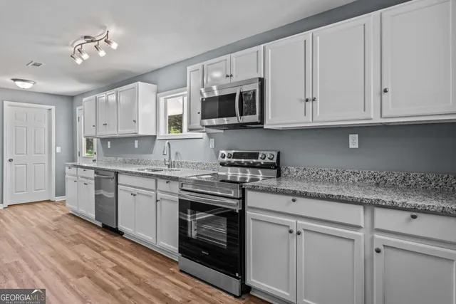 a kitchen with granite countertop a sink cabinets stainless steel appliances and a window