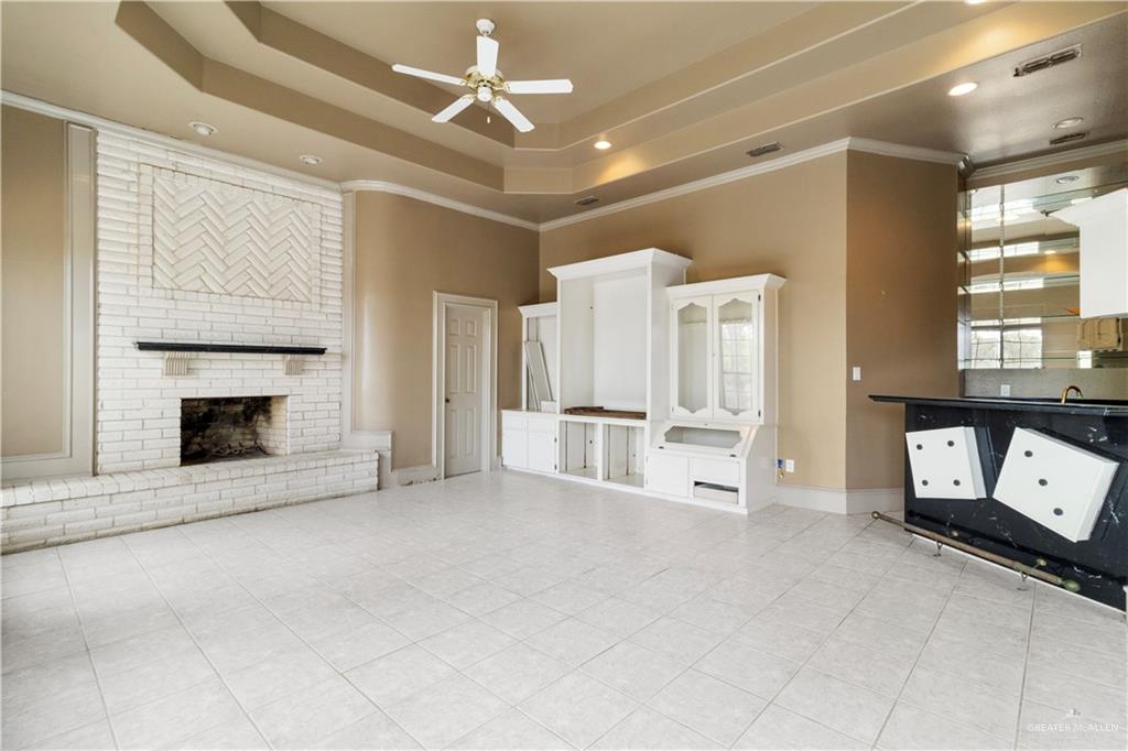 2107 South Victoria Road Donna, TX 78537 - Photo 5 of 25 Unfurnished living room featuring a ceiling fan, light tile patterned floors, a fireplace, a raised ceiling, and a high ceiling