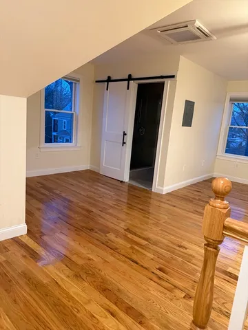 a view of an empty room with wooden floor and kitchen view