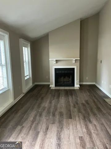 an empty room with wooden floor fireplace and windows