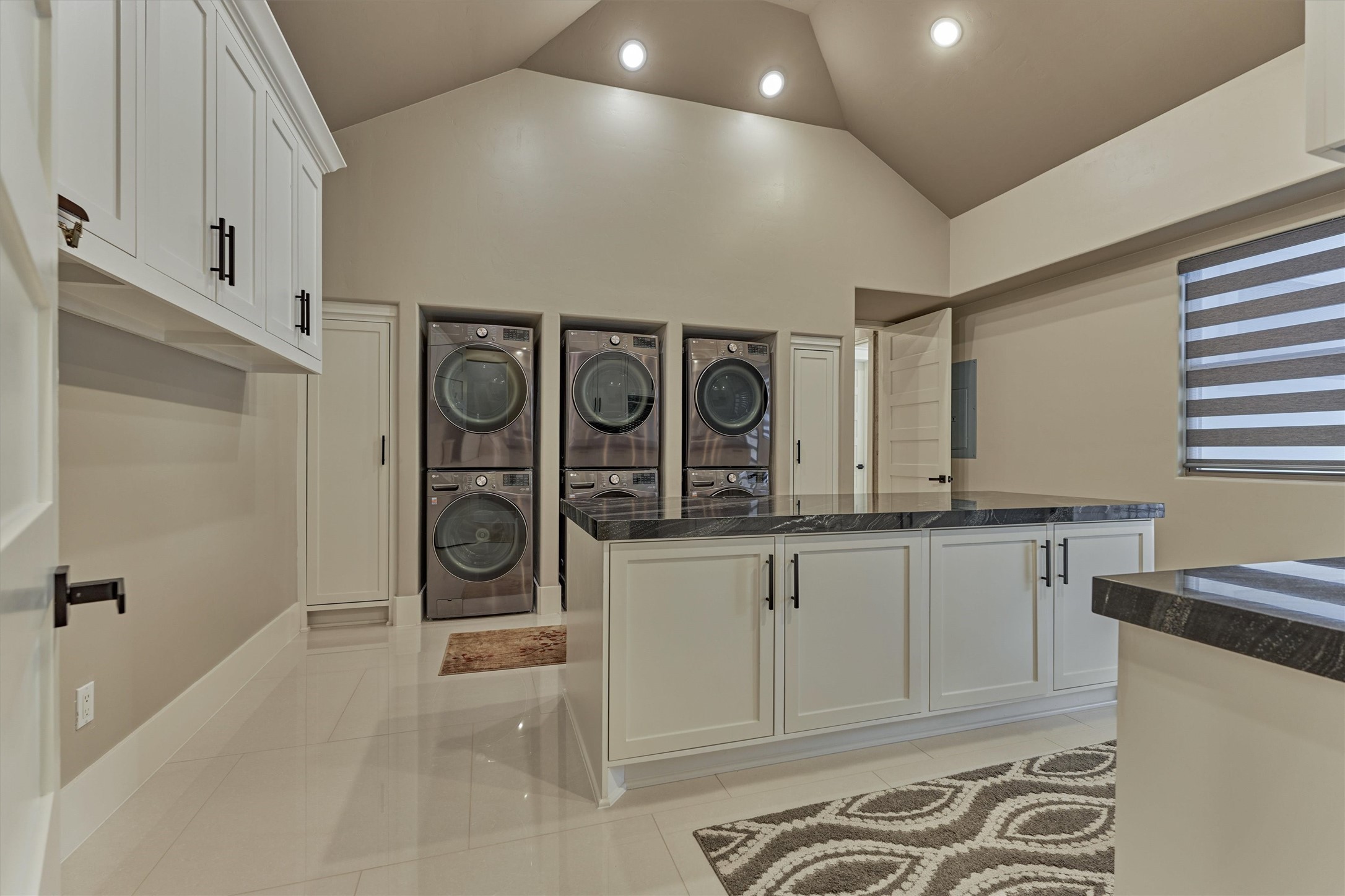 1907 Woerner Road Houston, TX 77090 - Photo 26 of 50 Where luxury meets practicality—this beautifully appointed laundry room showcases three washer and dryer sets, a custom storage island, and exquisite quartzite countertops for a refined finishing touch.