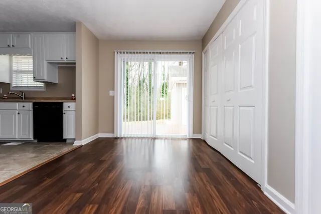 a view of a kitchen from an empty room with wooden floor and a window