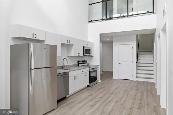 a kitchen with stainless steel appliances a refrigerator a sink and white cabinets