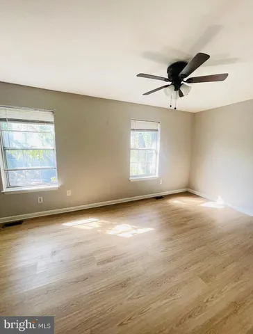 an empty room with wooden floor fan and windows