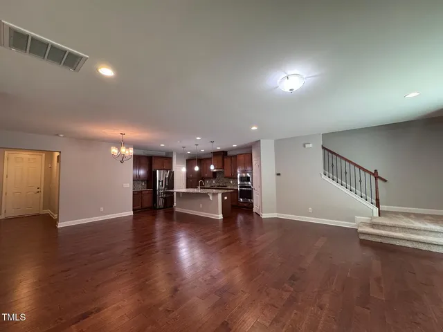 an empty room with wooden floor and a kitchen