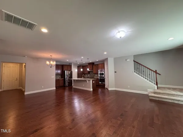 an empty room with wooden floor and a kitchen