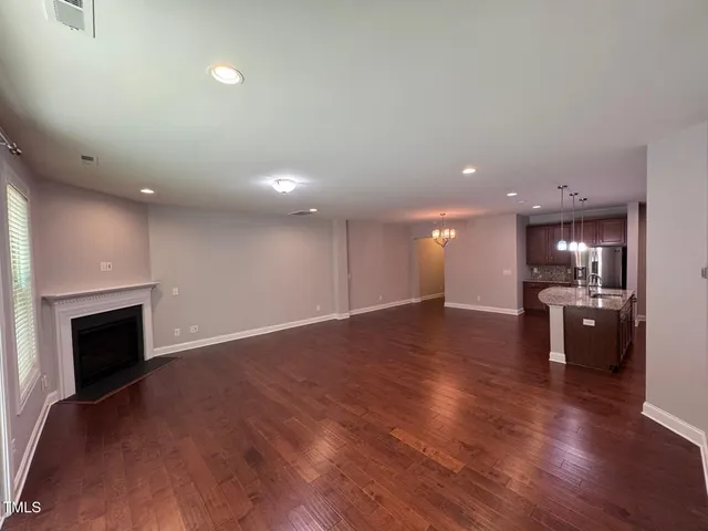 an empty room with wooden floor kitchen view and a fireplace