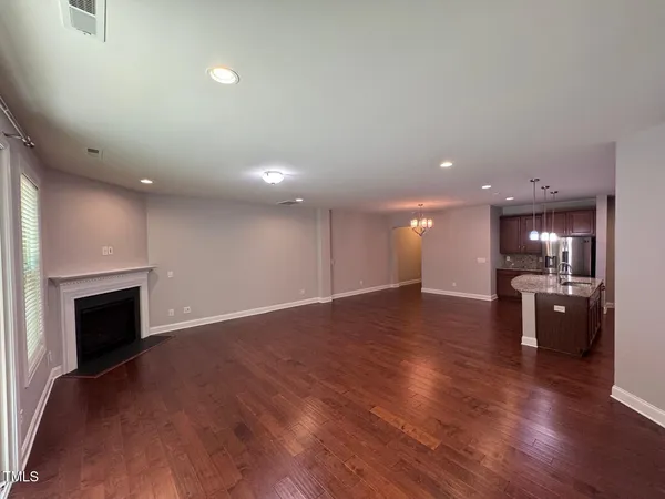 an empty room with wooden floor kitchen view and a window